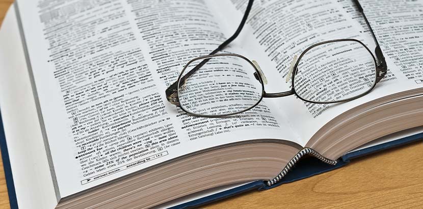 Ein aufgeschlagenes Wörterbuch, auf dem eine Brille liegt.