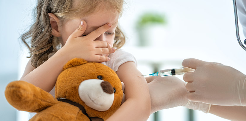 Eine Grippe-Impfung bei einem jungen Mädchen mit Teddy Bär.