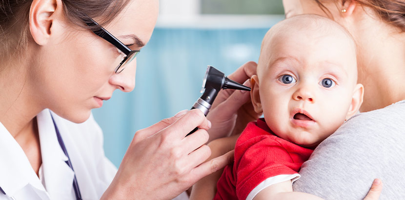Eine Ärztin untersucht Ohr, Mund und Nase von einem Baby.