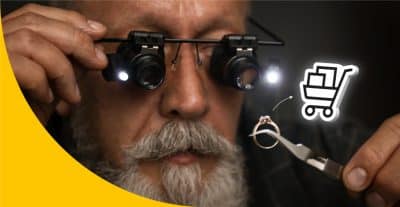 Juwelier in Nahaufnahme, der sich mit Lupenbrille einen Ring ansieht. Von diesem Ring führt ein Pfeil in Richtung eines Online Shop Symbols.