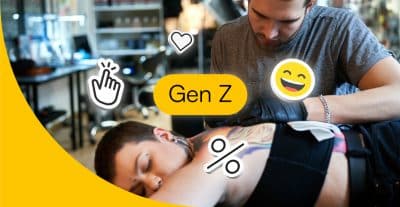 Tätowierer bei der Arbeit. Um ihn herum ein Emoji, ein Prozentzeichen und ein Herzsymbol. Dabei steht auch das Wort "Gen Z".